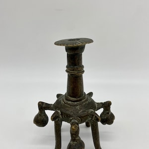 Puede incluir: Un pequeño candelero antiguo de bronce con una base redonda y cinco patas. Cada pata tiene un extremo bulboso. El candelero tiene un tallo cilíndrico y una parte superior redonda.