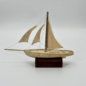 May include: A small wooden sailboat model with white sails, mounted on a dark wood base.