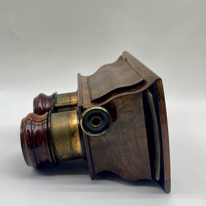 May include: Antique wooden binoculars with brass accents and a wooden case. The binoculars have a green and gold finish and are in good condition.