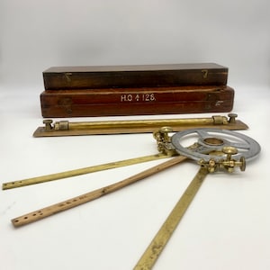 May include: A vintage brass and wood nautical navigation tool set in a wooden box. The set includes a protractor, a ruler, and a compass. The box is labeled "H.O. 126."