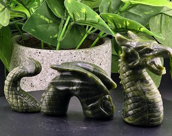 May include: Three green jade dragon sculptures. The dragons are carved in a realistic style with detailed scales and claws. The dragons are different sizes, with the largest dragon being about 6 inches tall.