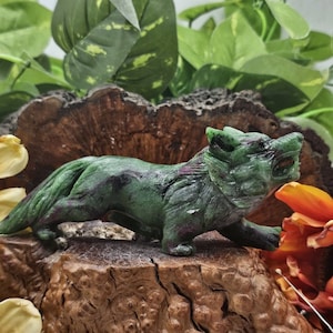 May include: A green and purple jade wolf sculpture with a snarling expression. The wolf is carved in a realistic style and has a detailed mane and tail.