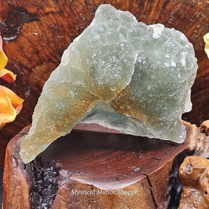 May include: A large, green and gold fluorite crystal with a rough, natural texture. The crystal is sitting on a wooden stand.