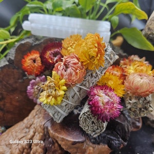 May include: White sage smudge sticks wrapped with dried flowers in shades of orange, yellow, pink, and purple. The flowers are arranged in a bouquet-like shape.