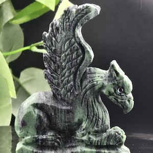 May include: A detailed sculpture of a griffin, a mythical creature with the body of a lion and the head and wings of an eagle. The statue is carved from a green and black stone, with intricate feather and muscle details. The griffin is in a seated position.