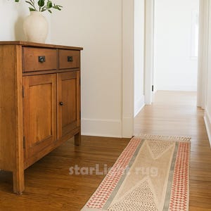 May include: A rectangular rug with a geometric design in a hallway. The rug features a beige central field with a dotted pattern and a red and white border. The rug has fringe on both ends. The text "starLight rug" is visible.