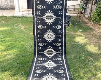 May include: A long, rectangular black and white patterned rug with a geometric design. The rug features a repeating pattern of white geometric shapes against a black background. The rug has a fringe at the bottom.