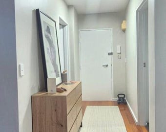 May include: A light wood dresser with six drawers in a hallway with white walls and a white door. The dresser is next to a white door and a white door with a window.