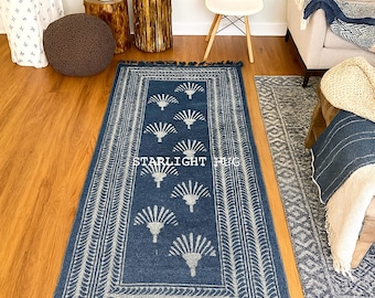 Op de afbeelding: Een rechthoekig blauw tapijt met een wit waaierpatroon en franjes. Het tapijt heeft een randontwerp en de tekst "STARLIGHT RUG" in het midden. Het tapijt ligt op een houten vloer.