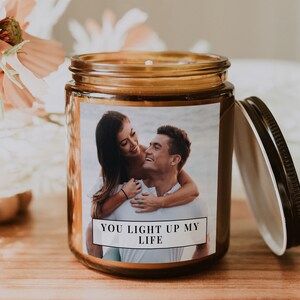 Op de afbeelding: Een bruine glazen kaars pot met een wit label. Het label heeft een foto van een stel dat lacht en de tekst "You light up my life".