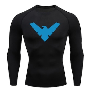Peut inclure: T-shirt de compression noir à manches longues avec un logo d'oiseau bleu stylisé sur la poitrine. Le t-shirt a un col rond et des manches raglan. Le logo est un motif géométrique d'oiseau en vol.