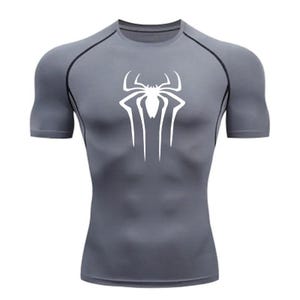 Puede incluir: Una camiseta de compresi&oacute;n de manga corta gris con un logotipo de Spiderman blanco en la parte delantera.