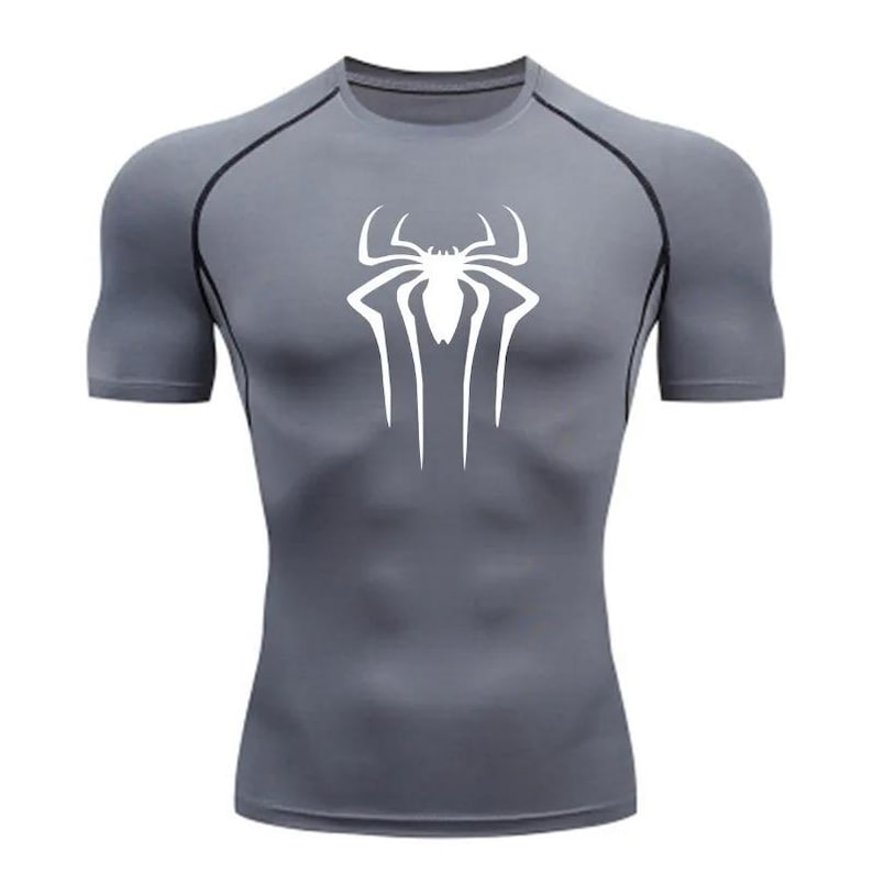 Puede incluir: Una camiseta de compresi&oacute;n de manga corta gris con un logotipo de Spiderman blanco en la parte delantera.