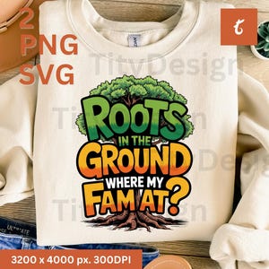 May include: Cream-colored sweatshirt with the text "Roots in the Ground Where My Fam At?" in a colorful, tree-themed design. The graphic features a tree with green leaves and a brown trunk. The sweatshirt is paired with blue jeans.