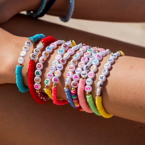 May include: A stack of colorful beaded bracelets with different words spelled out on each one. The words include "REPUTATION", "MILION", "FOLK", "EARN MORE", "LOVE", "SIGNA", and "EARLESS".