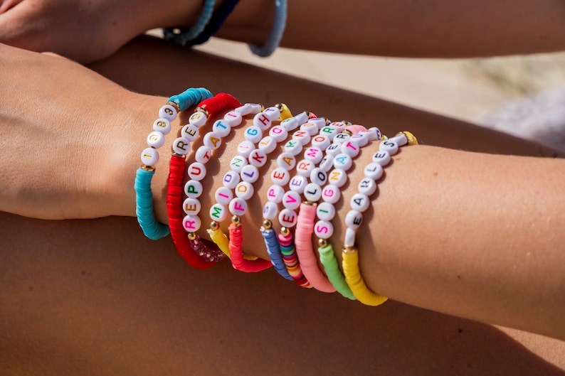 May include: A stack of colorful beaded bracelets with different words spelled out on each one. The words include "REPUTATION", "MILION", "FOLK", "EARN MORE", "LOVE", "SIGNA", and "EARLESS".
