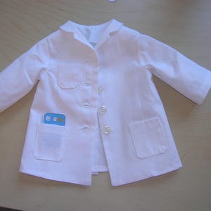 May include: A white lab coat with a pocket on the left side and a pocket on the right side. The coat has a button closure and a collar.