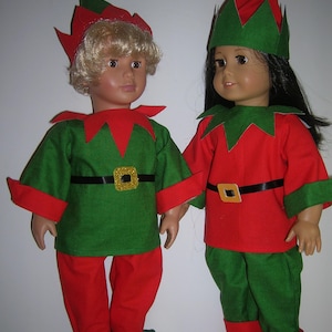 May include: Two elf dolls wearing green and red elf costumes with pointy hats. The dolls have blonde and black hair.