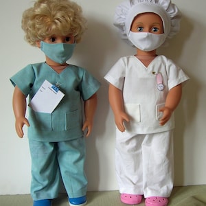 May include: Two dolls dressed in medical attire. The left doll has blonde curly hair, wears a teal scrub top with a patient notes pad clipped to the pocket, teal pants, and a matching face mask. The right doll wears a white scrub top, white pants, a white surgical cap, a white face mask, and pink clogs.