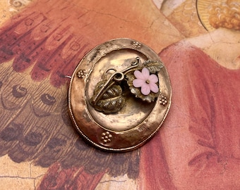 May include: A vintage gold-toned brooch with a delicate floral design. The brooch features a pink flower with a gold centre and two gold leaves.
