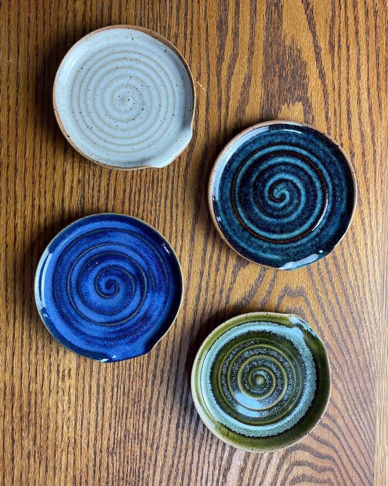 May include: Four ceramic spoon rests with a swirl design. One is white with brown speckles, one is blue with a dark blue swirl, one is dark blue with a light blue swirl, and one is green with a light green swirl.