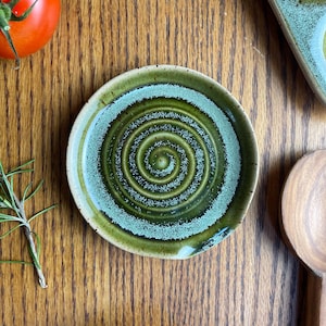 May include: A green and white ceramic spoon rest with a swirling pattern. The spoon rest is on a wooden surface.
