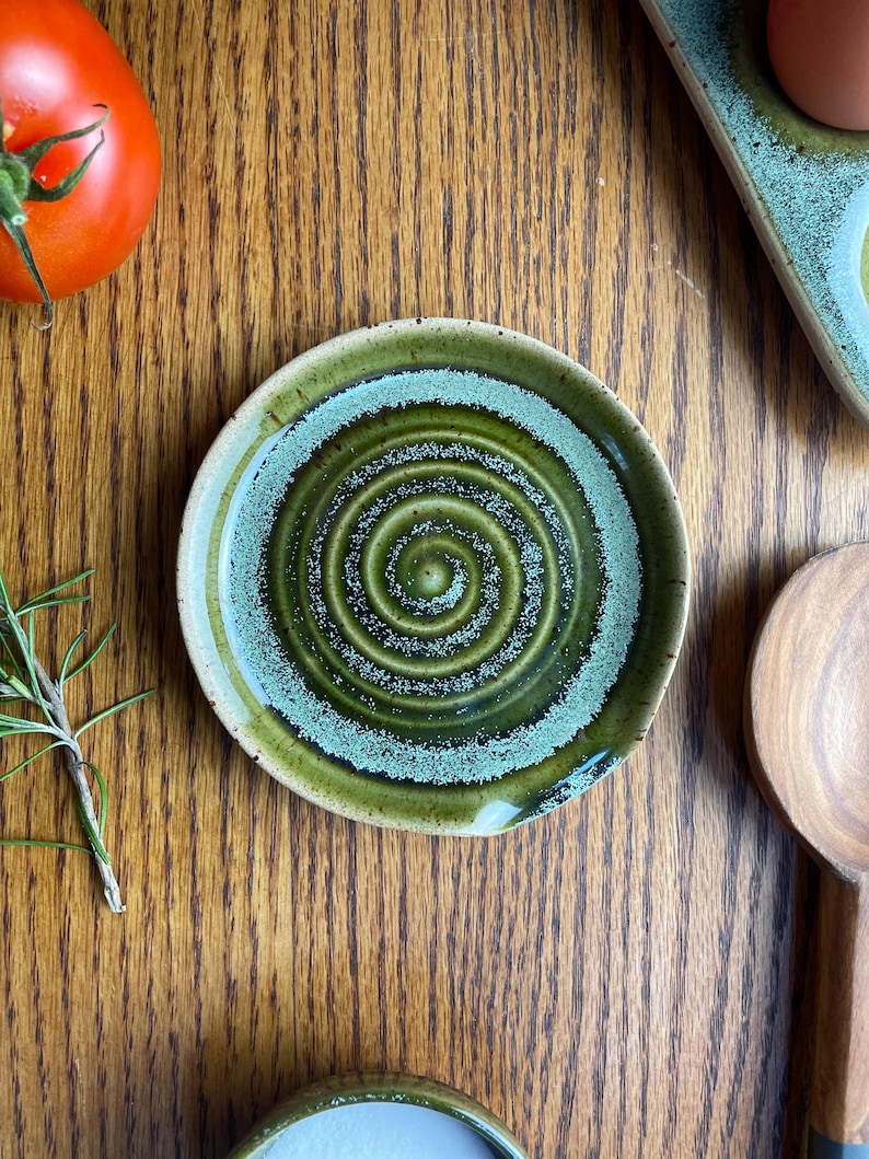 May include: A green and white ceramic spoon rest with a swirling pattern. The spoon rest is on a wooden surface.