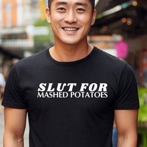 Op de afbeelding: Een zwart T-shirt met witte tekst die "Slut for Mashed Potatoes" zegt.