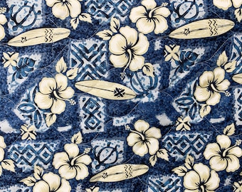 Op de afbeelding: Een blauwe en witte stof met een Hawaïaans thema. Het patroon bevat hibiscusbloemen, surfplanken en schildpadden.