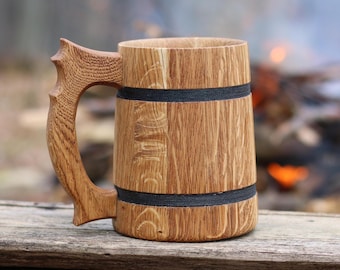 May include: A wooden beer mug with a handle and two black bands around the body. The mug is made of light brown wood and has a rustic look.