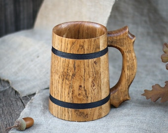May include: A wooden beer stein with a black band around the middle and a wooden handle. The stein is sitting on a piece of burlap fabric.