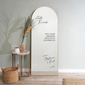 Può includere: Un grande specchio ad arco con cornice dorata. Lo specchio presenta il testo "Hello Friends" e "YOU LOOK AMAZING. NOW LET'S CELEBRATE.". Sotto il testo c'è "xoxo, Stephanie & Paul 12.07.2025".