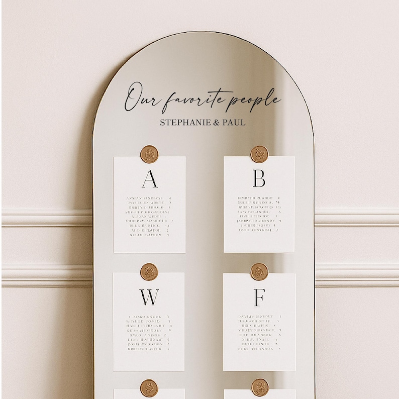 May include: A mirrored seating chart with an arched top. The text "Our favorite people" and "Stephanie & Paul" are written in elegant script. White cards with guest names are affixed with gold wax seals.