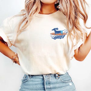 Woman wearing surfer dog pocket t-shirt at the beach with coastal background