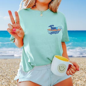 Light blue Comfort Colors shirt with small surfer dachshund pocket design on chest