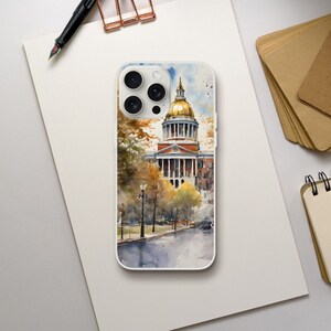 May include: A watercolor painting of a building with a gold dome, surrounded by trees and a street. The building is a light brown color with white trim and windows. The trees are green and yellow, and the street is gray. The painting is on a white phone case.