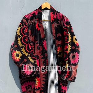 Pode incluir: Uma longa bata de veludo preto com um padrão floral em tons de vermelho, rosa e amarelo. A bata tem um forro listrado e está pendurada em um cabide de madeira.