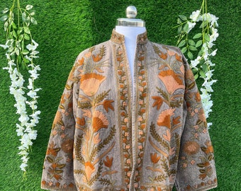 May include: A taupe-coloured jacket featuring a mandarin collar and long sleeves, adorned with intricate floral embroidery in shades of burnt orange, mustard yellow, and olive green. The garment has an open front design with detailed stitching.