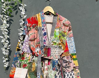 May include: A colorful patchwork kimono with a black and white striped sash. The kimono is made of various fabrics with floral and animal prints. The kimono is hanging on a hanger against a gray wall.
