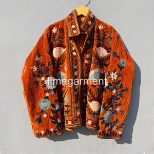 May include: A burnt orange velvet jacket with intricate floral embroidery in shades of blue, green, and pink. The jacket has a mandarin collar and a button closure.