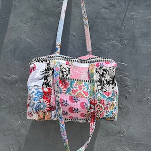 Może przedstawiać: Torba typu tote w stylu patchwork z kwiatowym nadrukiem w odcieniach różowego, niebieskiego, czarnego i białego. Torba ma długi pasek i zamek błyskawiczny.