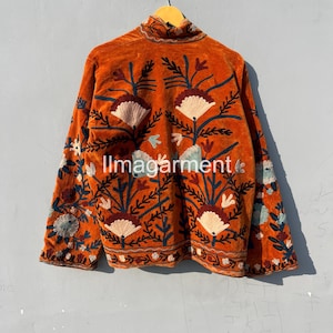 May include: A burnt orange velvet jacket with intricate floral embroidery in shades of blue, green, and pink. The jacket has a high neck and long sleeves.