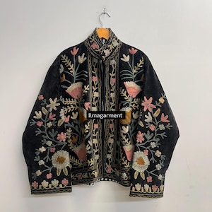 Pode incluir: Casaco preto bordado com gola alta e fecho de correr completo. O casaco apresenta bordados florais coloridos em rosa, amarelo e verde. O texto "Ilmagarment" é visível.