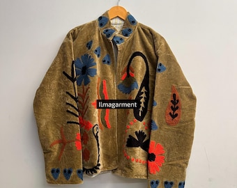 May include: A tan velvet jacket with colorful floral embroidery. The jacket features a high collar and a zipper closure. The embroidery includes blue, red, and black floral designs, with the text "Ilmagarment" visible on the front.