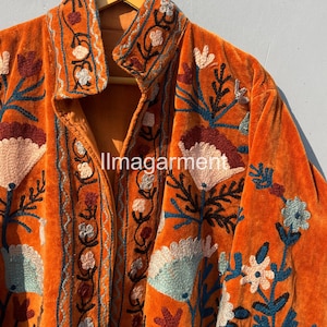 May include: A burnt orange velvet jacket with intricate floral embroidery in shades of blue, green, pink, and brown. The jacket has a button-up front and a collar.