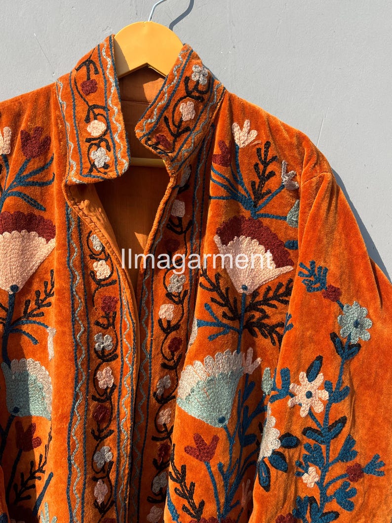 May include: A burnt orange velvet jacket with intricate floral embroidery in shades of blue, green, pink, and brown. The jacket has a button-up front and a collar.