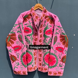 May include: Pink embroidered jacket with floral and leaf designs in red, green, and brown. The jacket has a collared neckline and a striped lining. The text "llmagarment" is visible on the front.