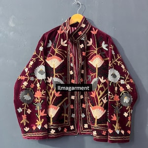 Könnte beinhalten: Burgunderfarbene Samtjacke mit aufwendiger Blumenstickerei in Creme, Orange und Grau. Die Jacke hat einen hohen Kragen und einen durchgehenden Reißverschluss. Der Text "llmagarment" ist sichtbar.