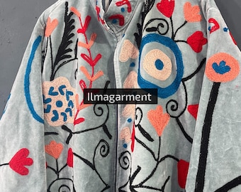 May include: A light blue jacket with intricate floral embroidery in red, orange, black, and blue. The jacket features a high collar and is hanging on a wooden hanger. The text "llmagarment" is visible on the jacket.