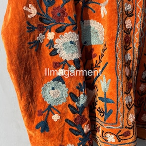 May include: Orange velvet jacket with intricate floral embroidery in shades of blue, pink, and green. The embroidery features a variety of flowers and leaves, creating a beautiful and intricate design.